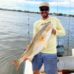 I am holding up a big redfish on a boat with houses in the background.
