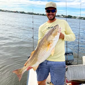 I am holding up a big redfish on a boat with houses in the background.