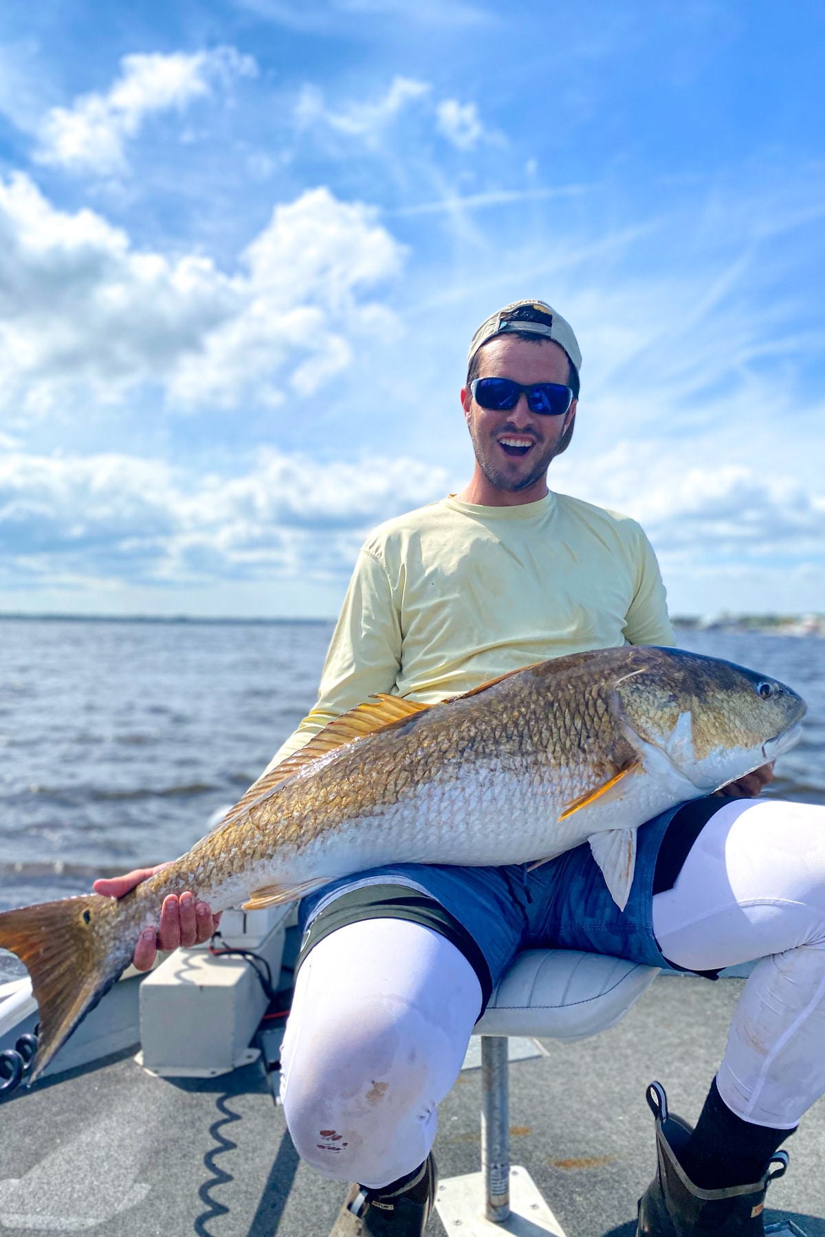 I am holding a giant bull redfish with a cloudy sky background.