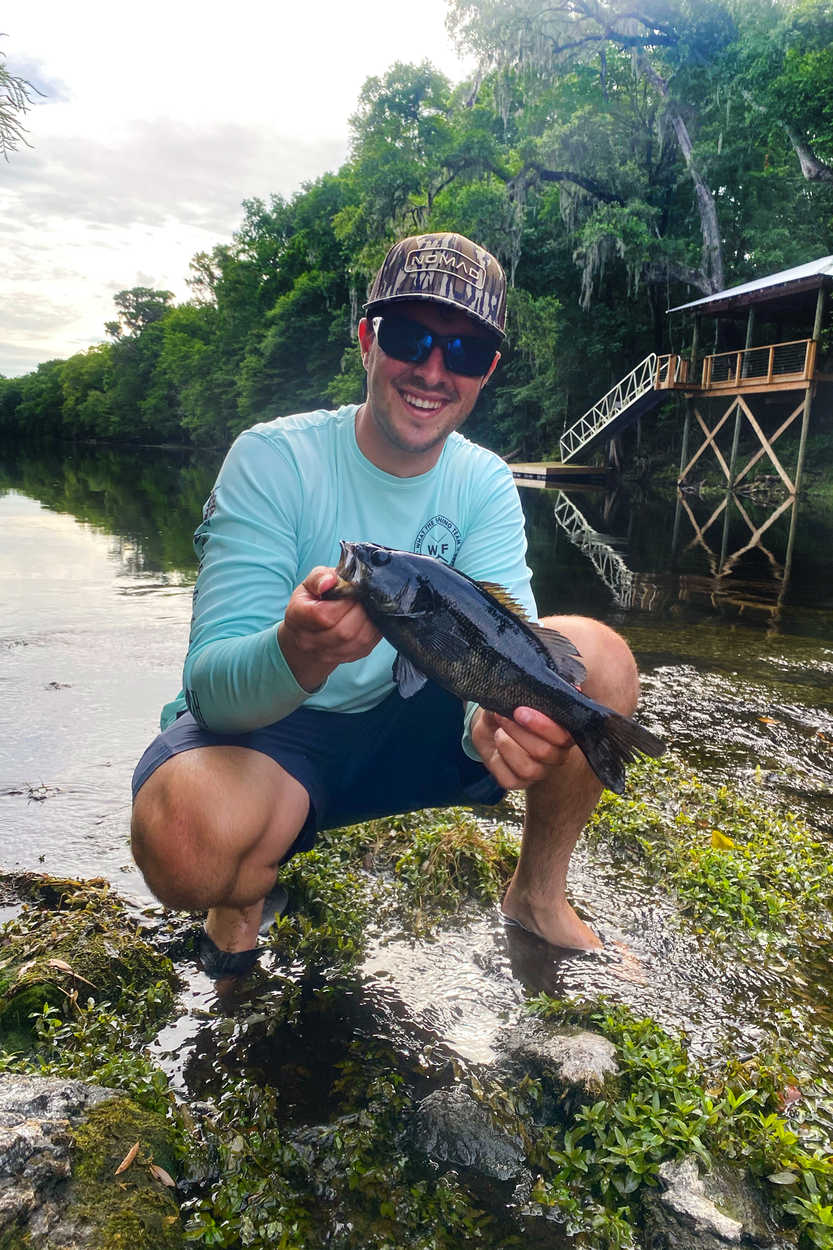 Holding a bass in a river with oak trees in the back ground. 